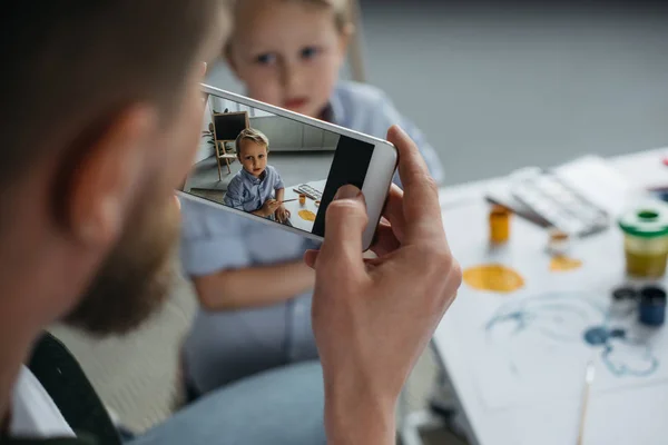 Vista parcial del hombre tomando fotos de hijos foto en el teléfono inteligente en casa - foto de stock