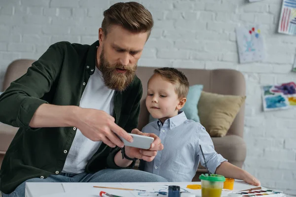 Man taking photo of sons picture on smartphone at home — Stock Photo