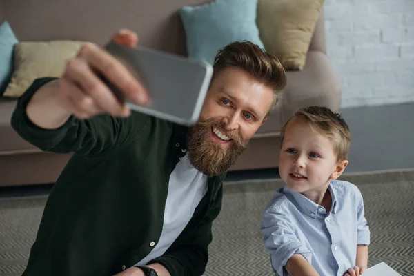 Smiling father and son taking selfie on smartphone together at home — Stock Photo