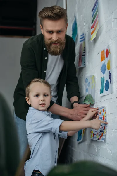 Familia colgando dibujo infantil en la pared juntos en casa - foto de stock