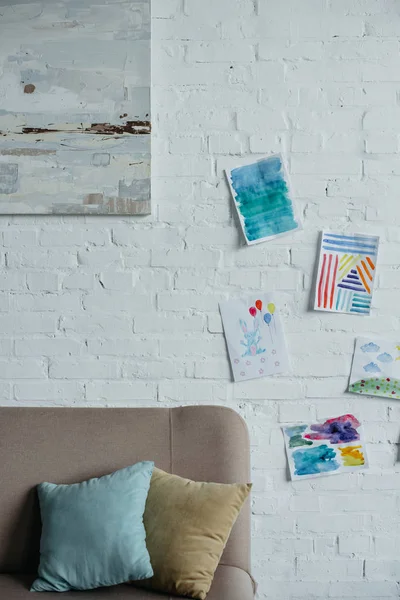 Vue rapprochée de la chambre d'enfant vide avec canapé et dessins colorés sur mur de briques blanches — Photo de stock