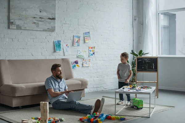 Pai com laptop sentado no chão com filho no quarto em casa — Fotografia de Stock