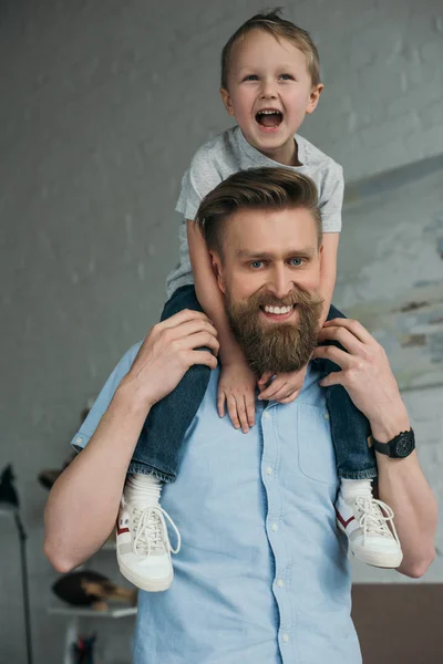 Lächelnder Vater mit kleinem Sohn auf Schultern, der zu Hause Spaß hat — Stockfoto