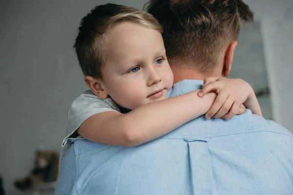 Cher petit garçon étreignant père et regardant loin à la maison — Photo de stock