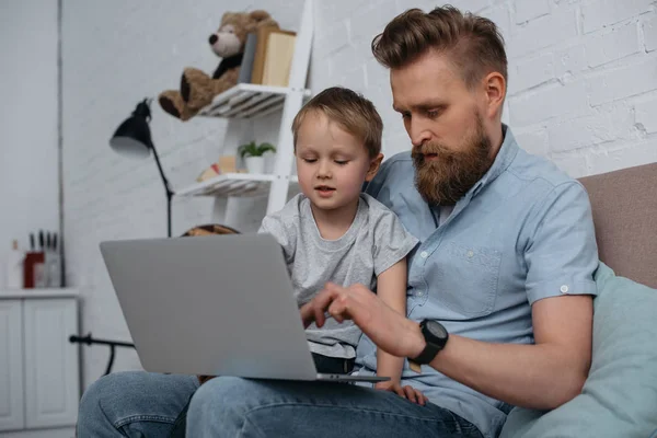 Focused father and son using laptop together at home — Stock Photo