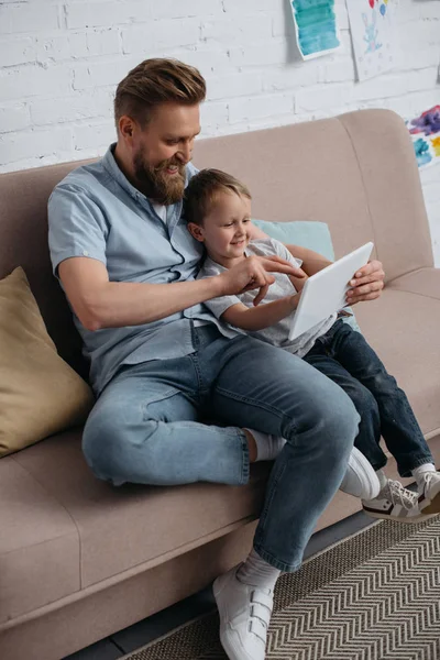 Pai e pequeno filho usando tablet juntos no sofá em casa — Fotografia de Stock