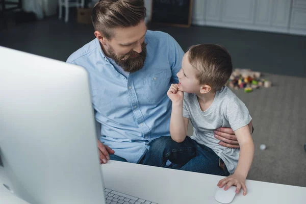 Vater und kleiner Sohn sitzen zu Hause am Tisch mit Computerbildschirm — Stockfoto