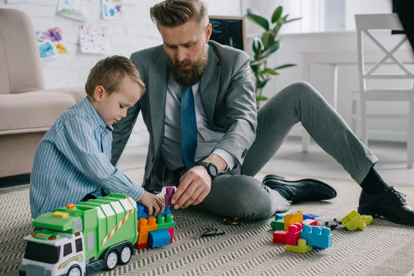 Geschäftsmann im Anzug und kleiner Sohn spielen zu Hause mit bunten Klötzen auf dem Boden, Arbeits- und Life-Balance-Konzept — Stockfoto