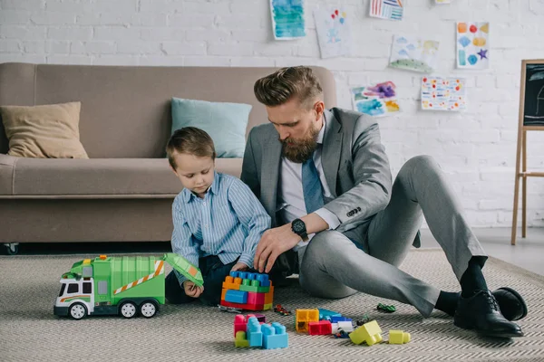 Uomo d'affari in giacca e cravatta e piccolo figlio giocare con blocchi colorati insieme sul pavimento a casa, il lavoro e concetto di equilibrio di vita — Foto stock