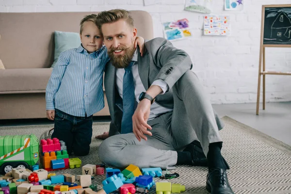 Niño abrazando sonriente padre en traje de negocios en casa, el trabajo y el equilibrio de la vida concepto - foto de stock