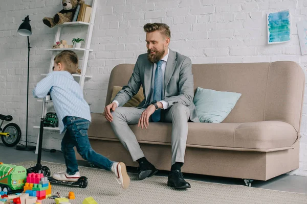 Geschäftsmann im Anzug und kleiner Sohn auf Motorroller zu Hause, Work-Life-Balance-Konzept — Stockfoto