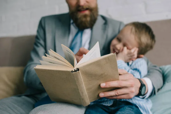 Selective focus of businessman and little son reading book together an sofa at home, work and life balance — Stock Photo