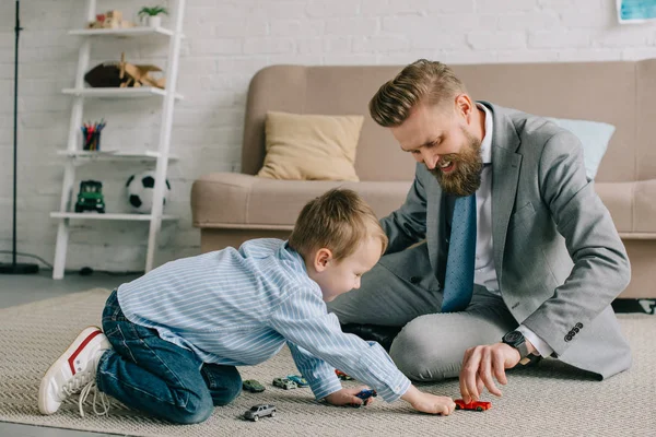 Businessman in suit and little son playing with toy cars on floor at home, work and life balance concept — Stock Photo