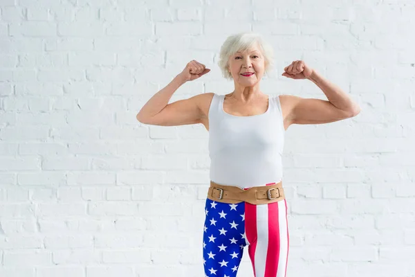 Glückliche Seniorin zeigt Muskeln und lächelt in die Kamera — Stockfoto