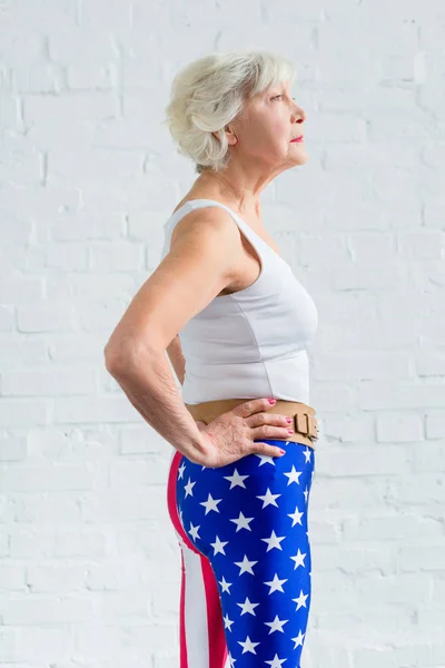 Seitenansicht einer Seniorin in Sportkleidung, die mit den Händen auf der Taille steht und wegschaut — Stockfoto