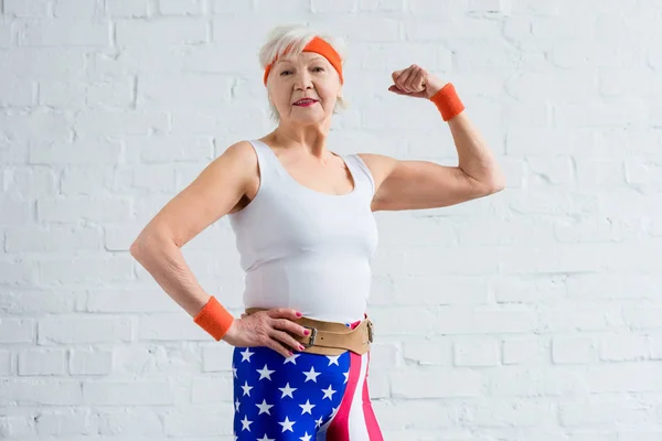 Happy senior sportswoman showing biceps and smiling at camera — Stock Photo