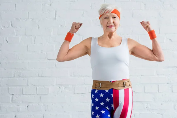 Happy senior sportswoman showing muscles and smiling at camera — Stock Photo