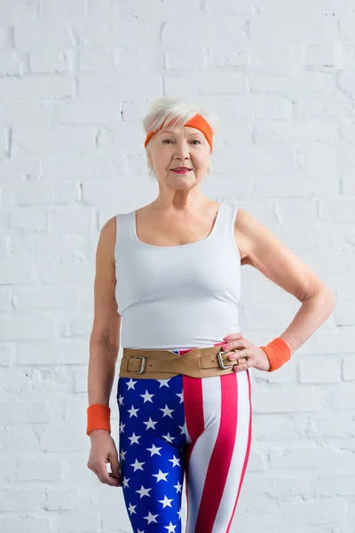 Heureuse sportive senior debout avec la main à la taille et souriant à la caméra — Photo de stock