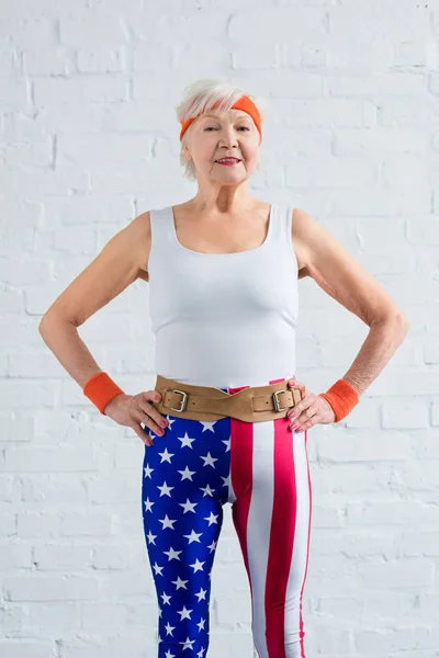 Heureuse sportive senior debout avec les mains sur la taille et souriant à la caméra — Photo de stock