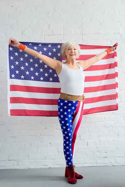 Happy senior sportswoman holding american flag and smiling at camera — Stock Photo