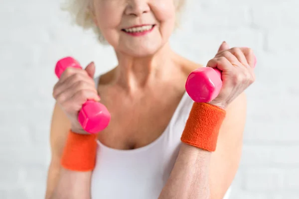 Cropped shot of smiling senior sportwoman holding dumbbells — Stock Photo