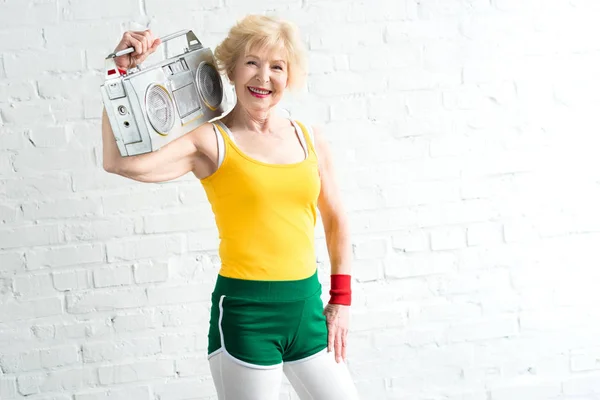 Fröhliche Seniorin hält Tonbandgerät in der Hand und lächelt in die Kamera — Stockfoto