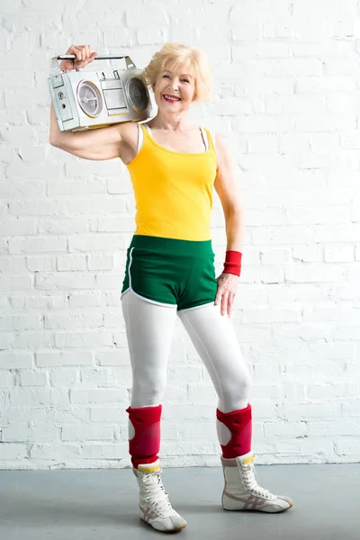 Hermosa deportista senior sosteniendo grabadora y sonriendo a la cámara — Stock Photo