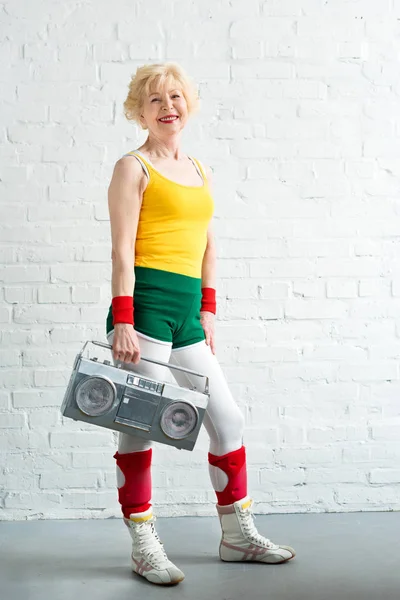 Hermosa deportiva mujer mayor sosteniendo grabadora y sonriendo a la cámara — Stock Photo