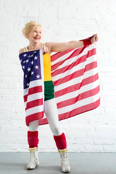 Счастливая спортивная пожилая женщина в костюме, держащая в руках наш флаг и отводящая взгляд — стоковое фото