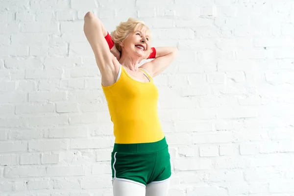 Cheerful sporty senior woman standing with hands behind head — Stock Photo