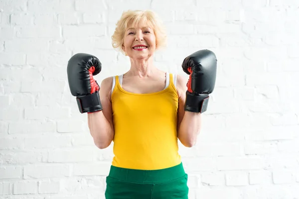 Heureuse femme âgée sportive en gants de boxe souriant à la caméra — Photo de stock