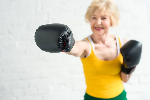 Вид крупным планом улыбающейся женщины в боксе в перчатках с селективной фокускопией — стоковое фото