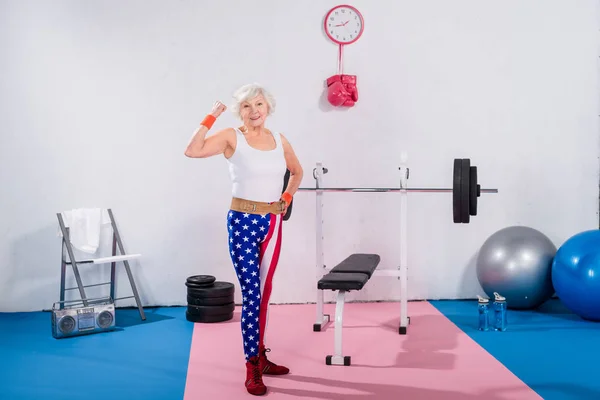 Спортивний старший леді в вітчизняної спортивний одяг показані м'язи і посміхається на камеру — стокове фото