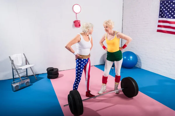 Hochwinkelaufnahme von älteren Sportlerinnen, die mit den Händen auf der Taille stehen und einander im Fitnessstudio anschauen — Stockfoto