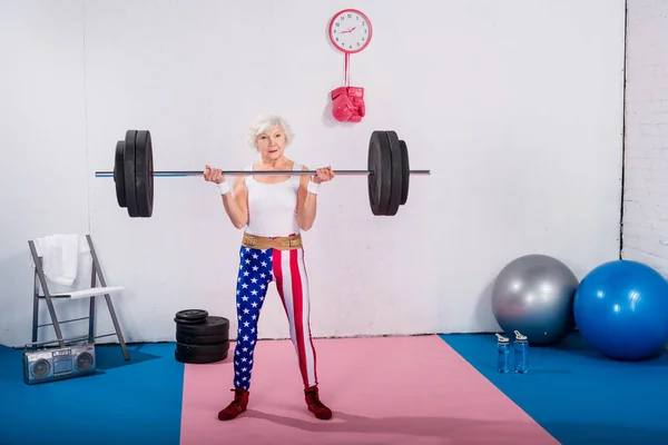 Sportliche Seniorin hebt Langhantel und blickt in Kamera — Stockfoto