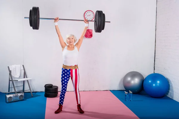 Sportive senior woman lifting barbell and smiling at camera — Stock Photo