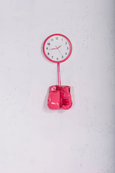 Pink boxing gloves hanging at pink wall clock on white — Stock Photo