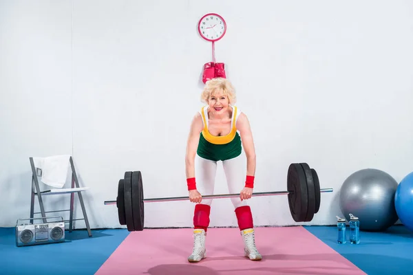 Felice anziana sportiva sollevamento bilanciere e sorridente alla macchina fotografica — Foto stock