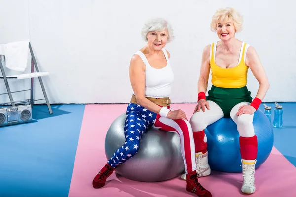 Sportliche Seniorinnen in Sportbekleidung sitzen auf Fitnessbällen und lächeln in die Kamera — Stockfoto