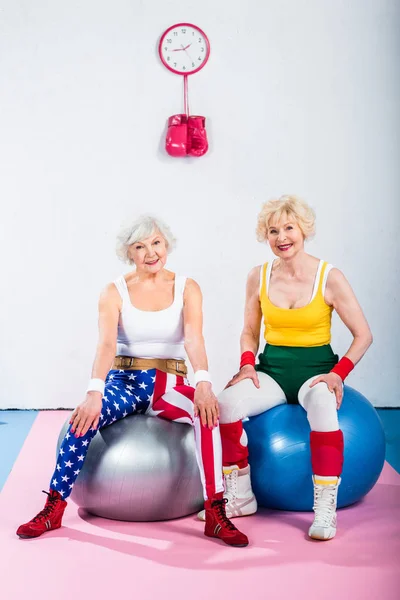 Deportivo senior las mujeres en sportswear sentado en fitness bolas y sonriendo a cámara — Stock Photo
