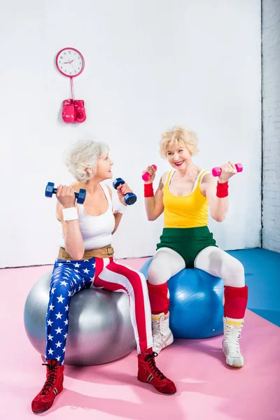 Sonriendo mujeres mayores en entrenamiento de ropa deportiva con mancuernas y sentado en bolas de fitness — Stock Photo