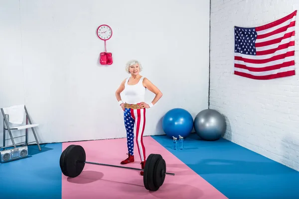 High angle view of patriotic senior sportswoman standing with hands on waist and smiling at camera — Stock Photo