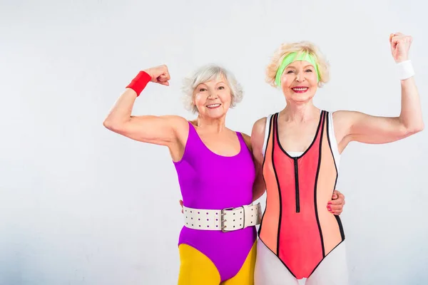 Feliz sénior deportistas mostrando los músculos y sonriendo a la cámara aislado en gris - foto de stock