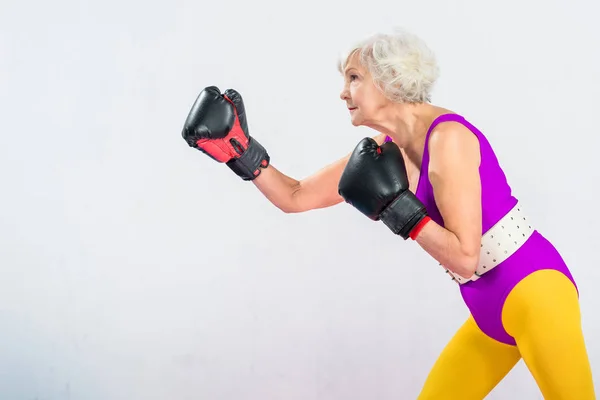 Vista laterale della signora anziana sportiva in boxe abbigliamento sportivo isolato su grigio — Foto stock