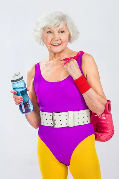 Beautiful smiling senior sportswoman holding bottle of water and boxing gloves — Stock Photo