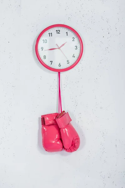 Vista da vicino dei guanti da boxe rosa appesi all'orologio da parete su bianco — Foto stock