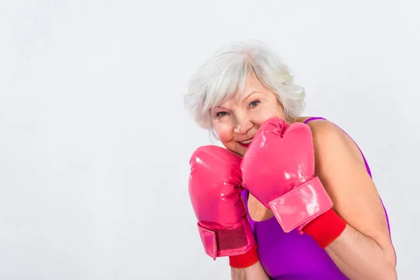 Beautiful senior woman in boxing gloves smiling at camera isolated on grey — Stock Photo