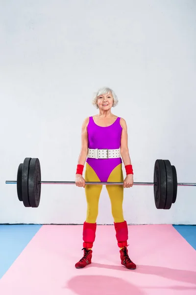 Sporty senior lady holding barbell and smiling at camera — Stock Photo