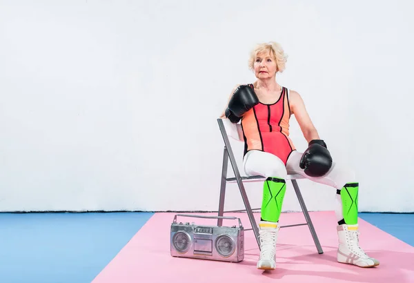 Mujer mayor deportiva en guantes de boxeo escuchando música y mirando hacia otro lado - foto de stock