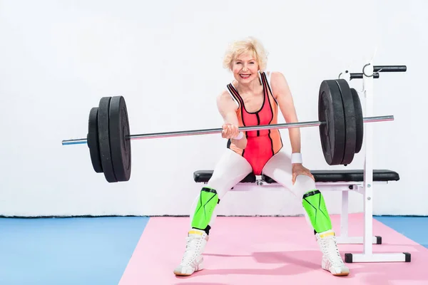 Happy senior sportswoman lifting barbell and smiling at camera — Stock Photo